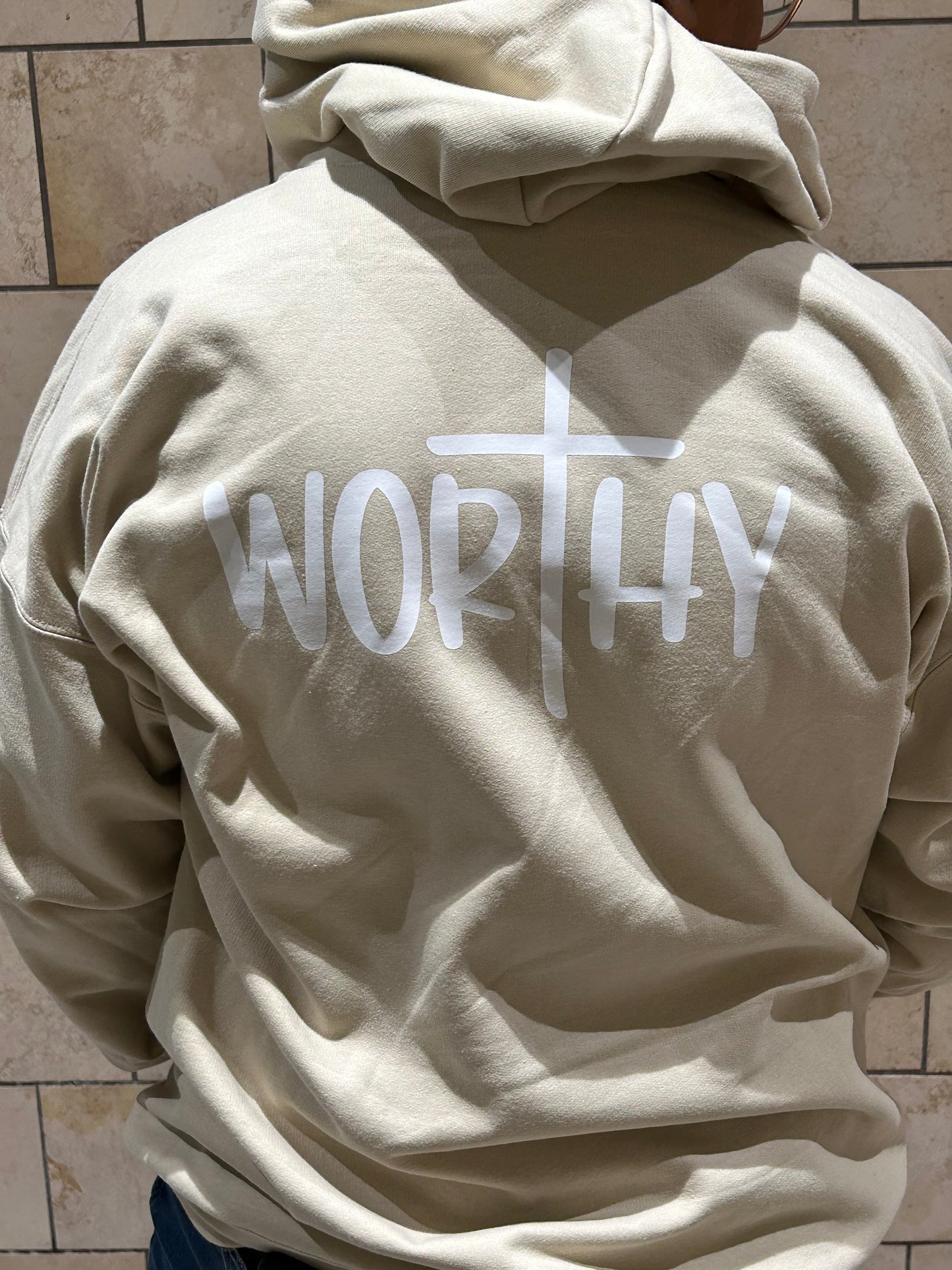 Close up of the hoodie in sand with the word "Worthy" on the back.